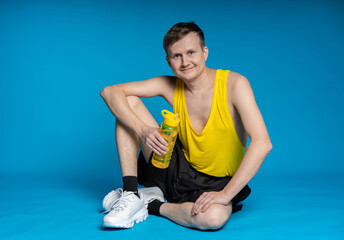 lean sportsman in a yellow t-shirt and black shorts on a blue background. sitting on the floor with...