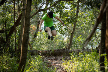Woman trail runner running and jumping over a fallen tree trunk in tropical forest mountain