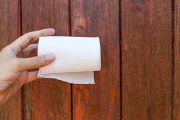 White toilet paper roll in female hand with space on wood background, cleaning product