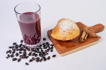 fried empanada with cheese next to a glass with purple api, corn drink, on a table with purple corn and cinnamon
