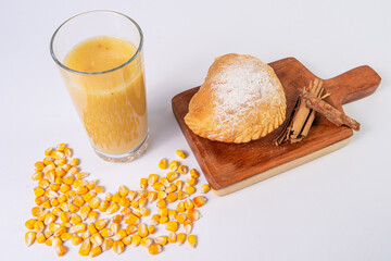 fried empanada with cheese next to a glass of corn drink, on a table with corn and cinnamon