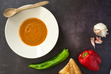 Andalusian gazpacho served in a white plate on a dark background. Tomato, pepper and fresh vegetable soup.