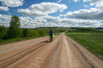 A cyclist rides along the road among the fields of Bashkiria, Ural, Russia.