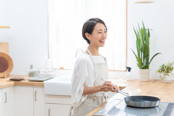 キッチンで料理をする笑顔のミドル女性（家事・主婦・自炊）