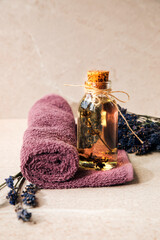 Lavender oil close-up on a violet towel with lavender flowers on a beige stone background. Front view