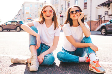 Two young beautiful smiling hipster female in trendy summer white t-shirt clothes and jeans.Sexy carefree women posing on the street background. Positive models having fun, hugging and going crazy
