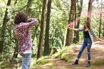 Anonymous profesional Photographer taking photographs of model in the forest holding a red smoke...