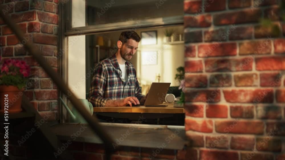 Leinwandbilder Male Software Engineer Coding on Laptop Computer while Working in Modern Apartment. Professional IT Specialist Designing Application. Remote Working Freelancer. View From Outdoors into Window.