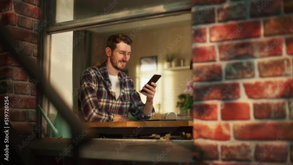 Poster happy smiling man sitting behind desk at home office and using smartphone. handsome man browsing thr