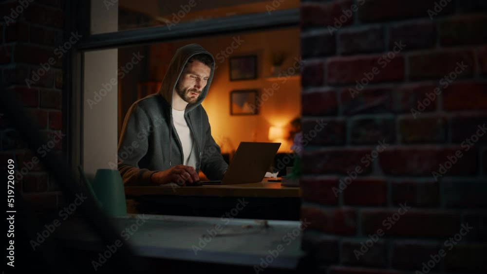 Aufkleber Professional Male Programmer Writing Code for New Project while Working Remotely on Laptop From Home Office. Freelance Software Engineer Designs App From his Apartment. View From Outdoors into Window.