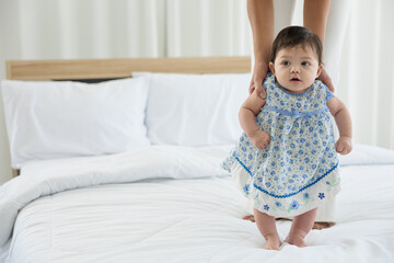 Fototapeta premium baby girl learning to walk and mother or sitter support her on bedroom