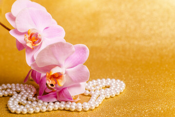 purple Orchid and pearl necklace on a shiny gold background

