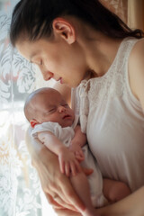 Mother holding her baby in her arms near the window