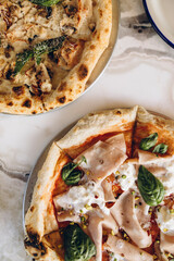 two pizzas close-up on a white marble table top view. Neapolitan pizza with burnt sides. pizza with italian sausage and pistachios