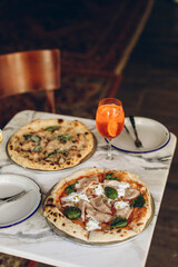 table setting in a pizzeria. two Italian pizzas with burnt sides and a cold summer cocktail on a marble table in a cafe. pizza with sausage, cheese and basil.
