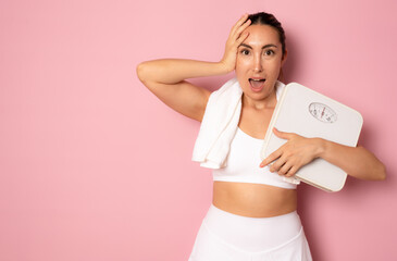 Worried young woman holding bathroom scales on pink background. Weight loss diet