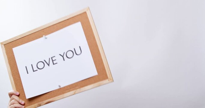 Woman's hand shows the paper on board with the word I LOVE YOU in white studio background with copy space.