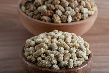 Bowl full of dried mulberry on a wooden background
