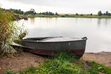 Naklejka na ściany i meble A motor boat is parked at the shore of a lake or river in the evening at sunset or early in the morning. The boat is in a quiet place next to the reeds and is ready for fishing.