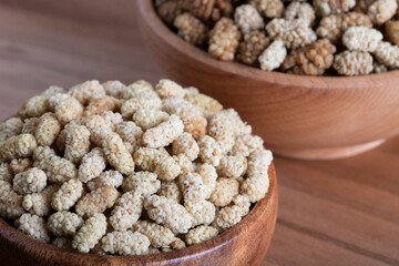 Bowl full of dried mulberry on a wooden background

