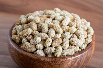 Bowl full of dried mulberry on a wooden background
