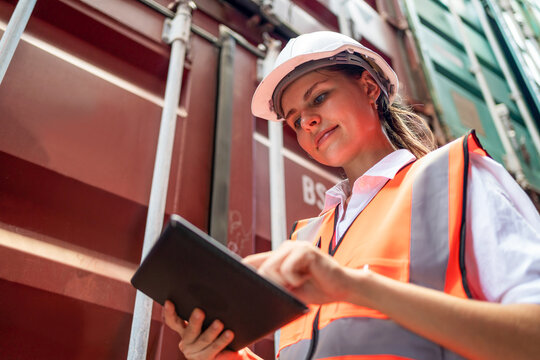 Dock manager or engineer worker in casual with vest standing in shipping container yard looking at tablet. Import and export product. Manufacturing transportation and global business concept