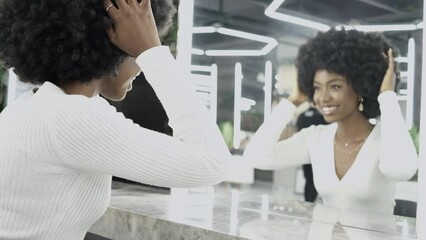 African American Woman fixing Her Curly Hair In Front Of Mirror in beauty salon