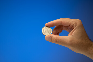 Fototapeta na wymiar 5 Swiss Francs metal coin, held in hand by a Caucasian male. Close up studio shot, isolated on blue background