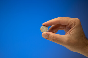 1 Swiss Francs metal coin, held in hand by a Caucasian male. Close up studio shot, isolated on blue...
