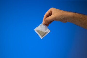 Single white paper tea bag held in hand by Caucasian male hand. Close up studio shot, isolated on...