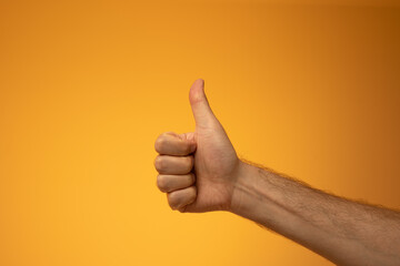 Thumbs up or OK sign made by Caucasian male hand. Close up studio shot, isolated on orange background