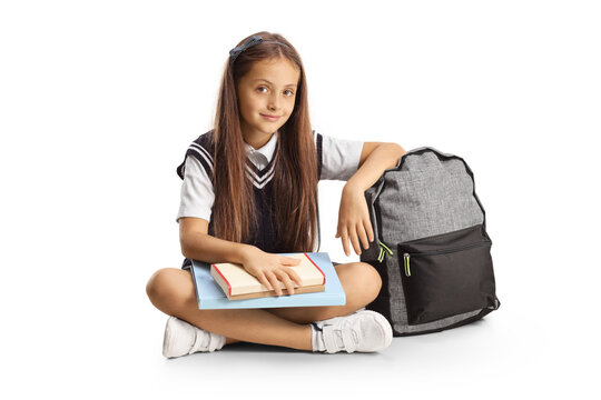 Schoolgirl sitting on the floor with a book on her lap and leaning on a backpack
