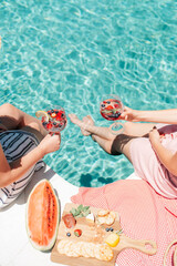Two friends / Ladies drinking Cocktails by a blue water pool in holiday resort