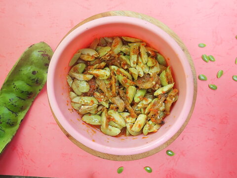 Homemade Indonesian traditional food chilli sauce parkia speciosa (sambal petai) in in a pink bowl on a red background.