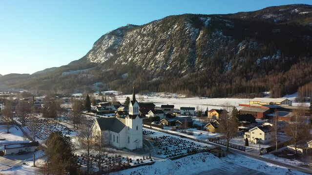 Nesbyen church during beautiful winter sunrise - Aerial moving around church with bright sunlight and sunflare background in middle of clip - Norway