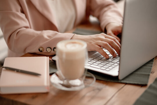 freelancer works on computer in cafe. girl, business woman in beige pink jacket is typing on the keyboard. coffee latte on the table. business lunch, online meeting. Business concept. selective focus