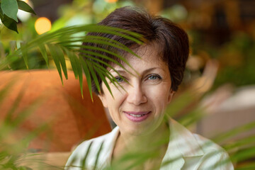 portrait of cute middle aged jewish woman in cozy green house. plant care. happy female smiling in...