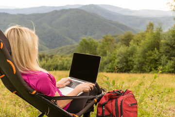 Young business woman working at the computer on the rock. Young girl downshifter working at a laptop at sunset or sunrise on the top of the mountain, working day.