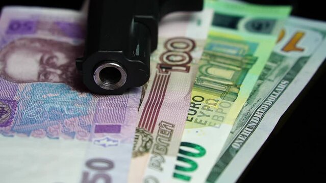 Pistol Gun on Ukrainian Hryvnia, Russian Rubles, Euro and US Dollars Banknotes. War Economy and Inflation Concept, Close Up