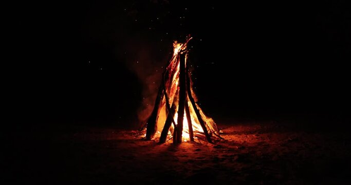 Blazing slow motion bonfire on a hidden beach during summer evening. Burning wood on white sand shore at sunset.