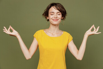 Young spiritual fun tranquil happy woman she 20s wear yellow t-shirt hold spreading hands in yoga...
