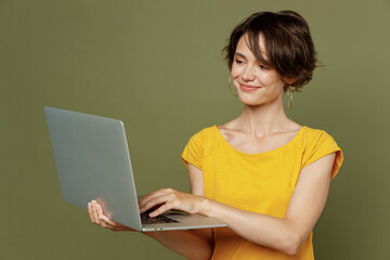 Young smiling freelancer programmer happy woman she 20s wear yellow t-shirt hold use work on laptop pc computer isolated on plain olive green khaki background studio portrait People lifestyle concept