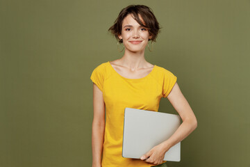 Young smiling freelancer confident programmer happy woman she 20s wear yellow t-shirt hold closed laptop pc computer isolated on plain olive green khaki background studio. People lifestyle concept