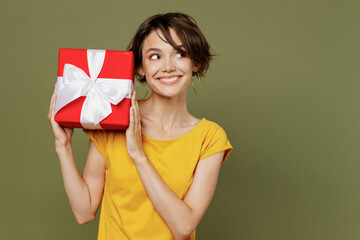 Young minded woman she 20s wear yellow t-shirt hold red present box with gift ribbon bow look aside on workspace area isolated on plain olive green khaki background studio People lifestyle concept.