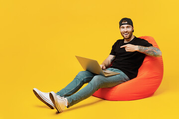 Full size young amazed bearded tattooed man 20s he wear casual black t-shirt cap sit in bag chair...