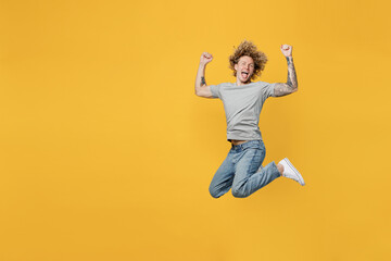 Fototapeta na wymiar Full body happy excited overjoyed young caucasian man 20s he wearing grey t-shirt look camera jump high do winner gesture isolated on plain yellow backround studio portrait. People lifestyle concept.