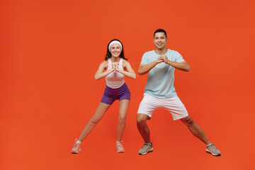 Fototapeta na wymiar Full size smiling fun young fitness trainer instructor sporty two man woman in headband t-shirt do squat spend weekend in home gym isolated on plain orange background. Workout sport lifestyle concept.