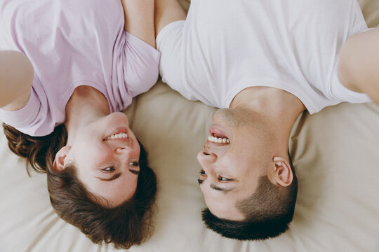 Upside down top view close up young couple two family man woman she he wear t-shirt pajama do selfie shot pov on mobile cell phone lying in bed rest spend time together in bedroom home in room hotel.