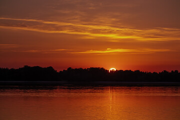 Naklejka premium Golden sunset over the river. The sun sets over the horizon, hides behind the trees