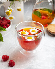 herbal tea with chamomile and berries on a light table in a summer style. the concept of tea drinking, herbal tea, proper nutrition, healthy drink